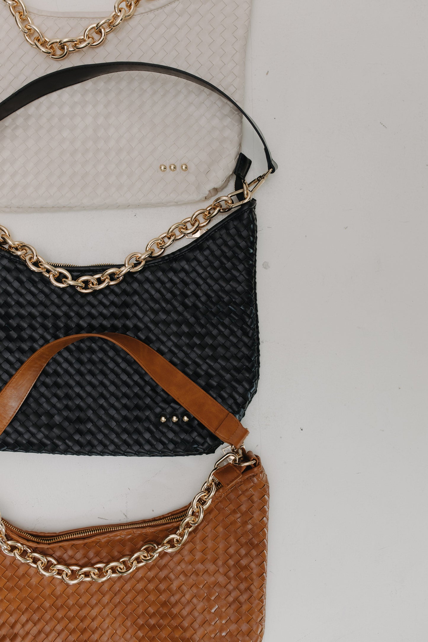 Three handbags, black, brown, cream with gold chains on a light gray background.