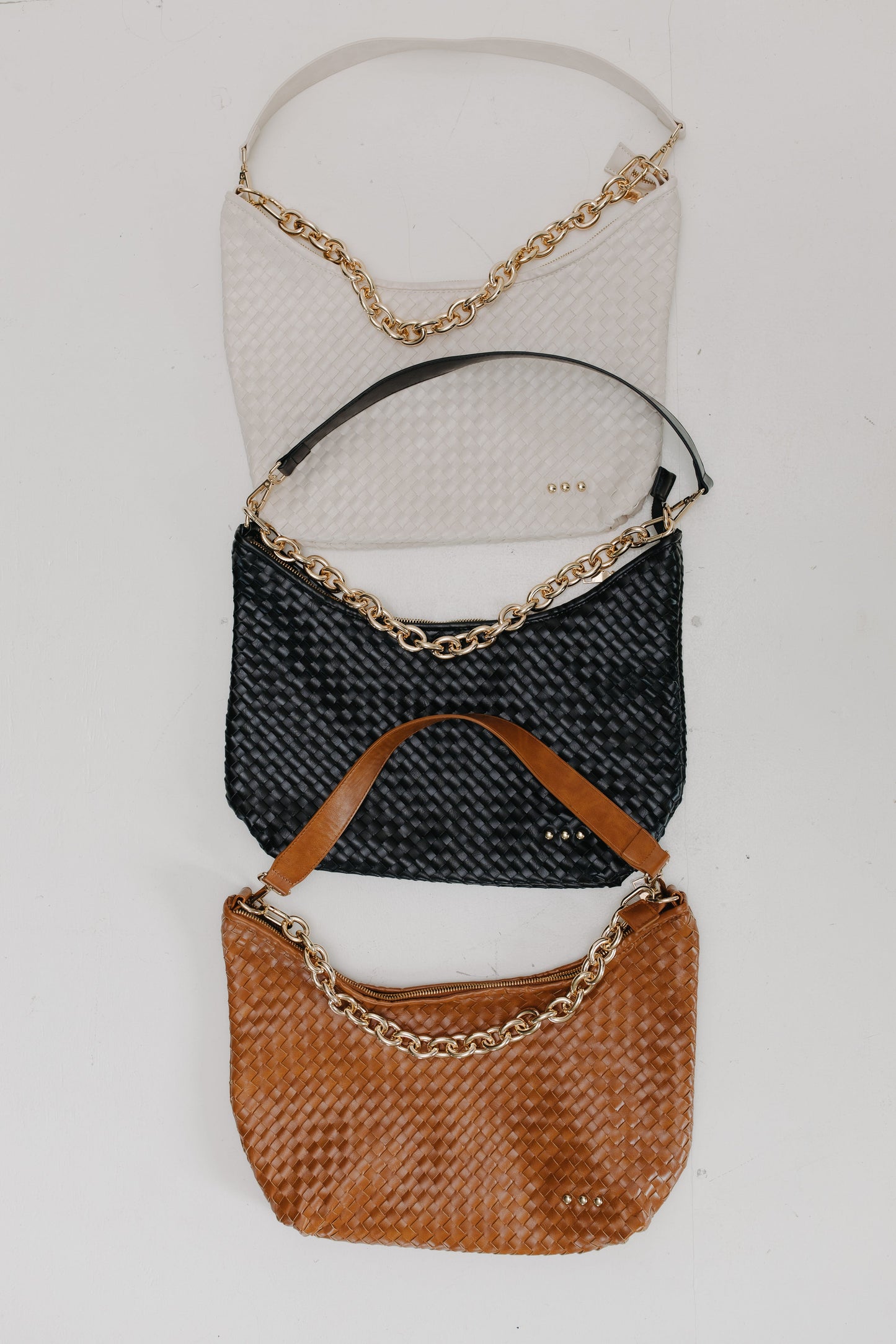 Three handbags in black, cream, and brown with gold chains on a light gray background