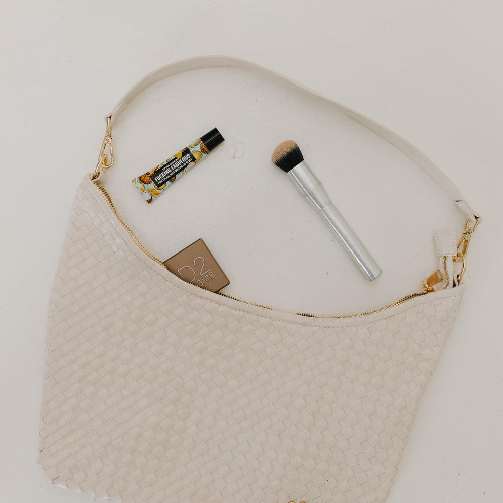 Cream handbag with makeup items on a white background