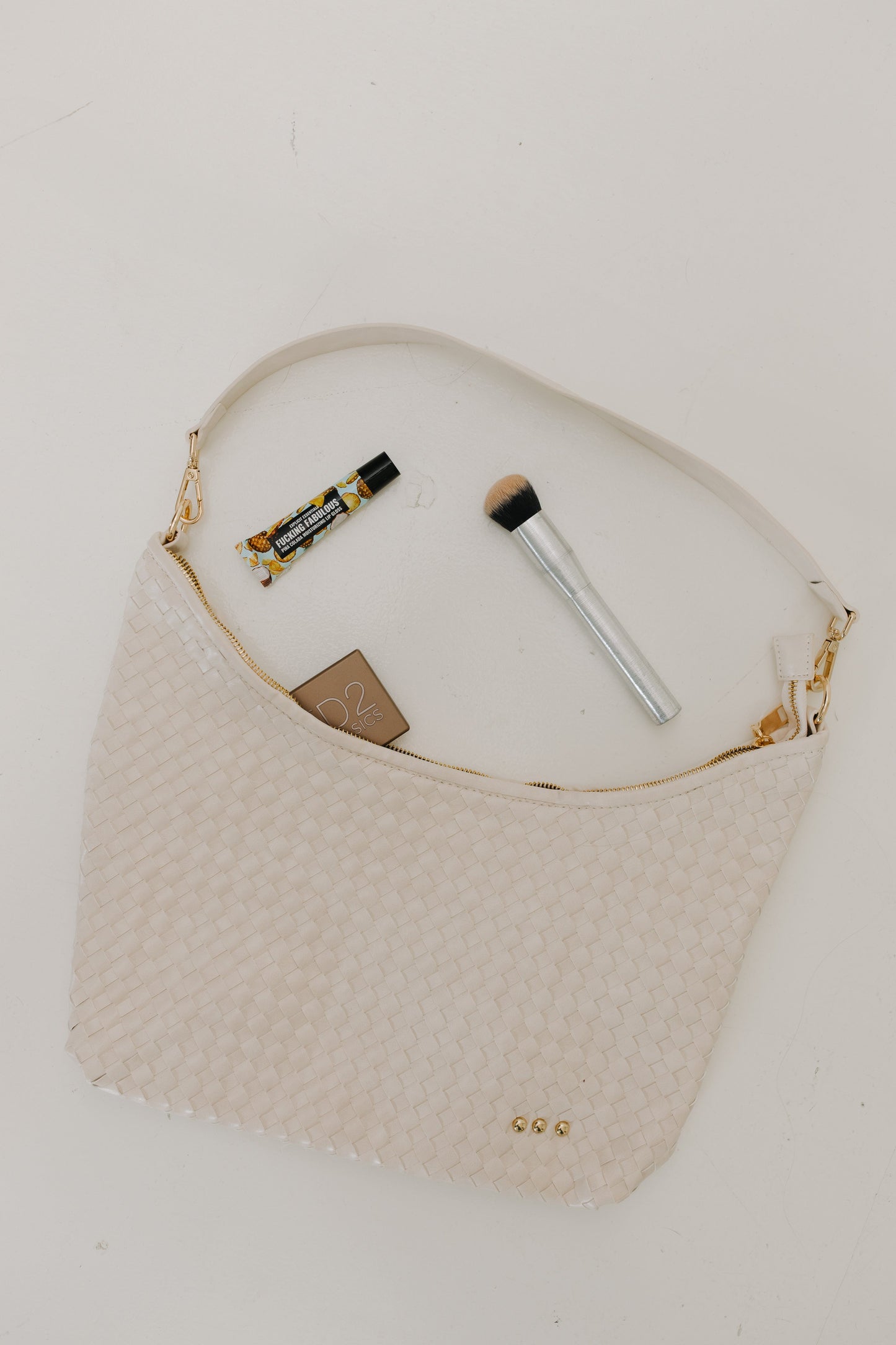 Cream handbag with makeup items on a white background