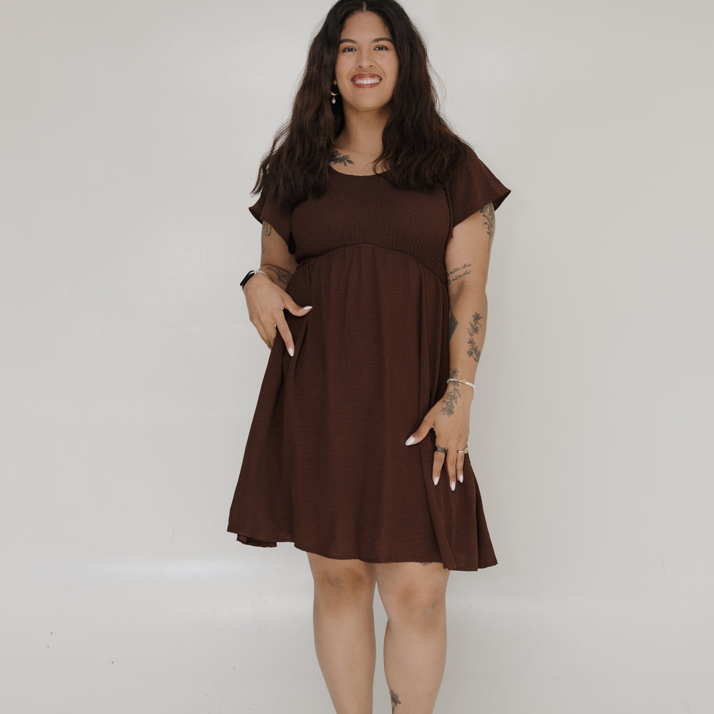 Woman wearing a brown dress standing against a white wall