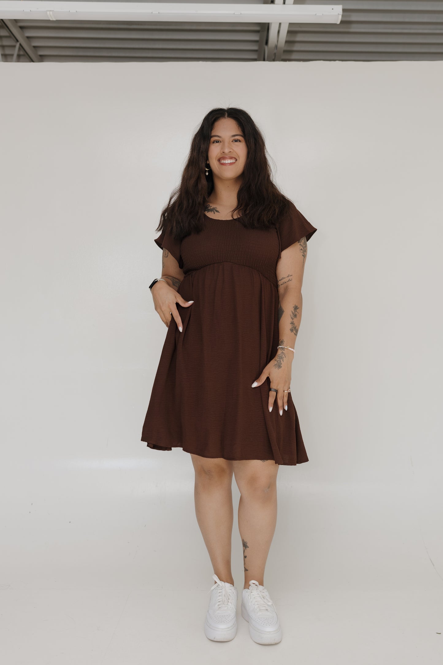 Woman wearing a brown dress standing against a white wall