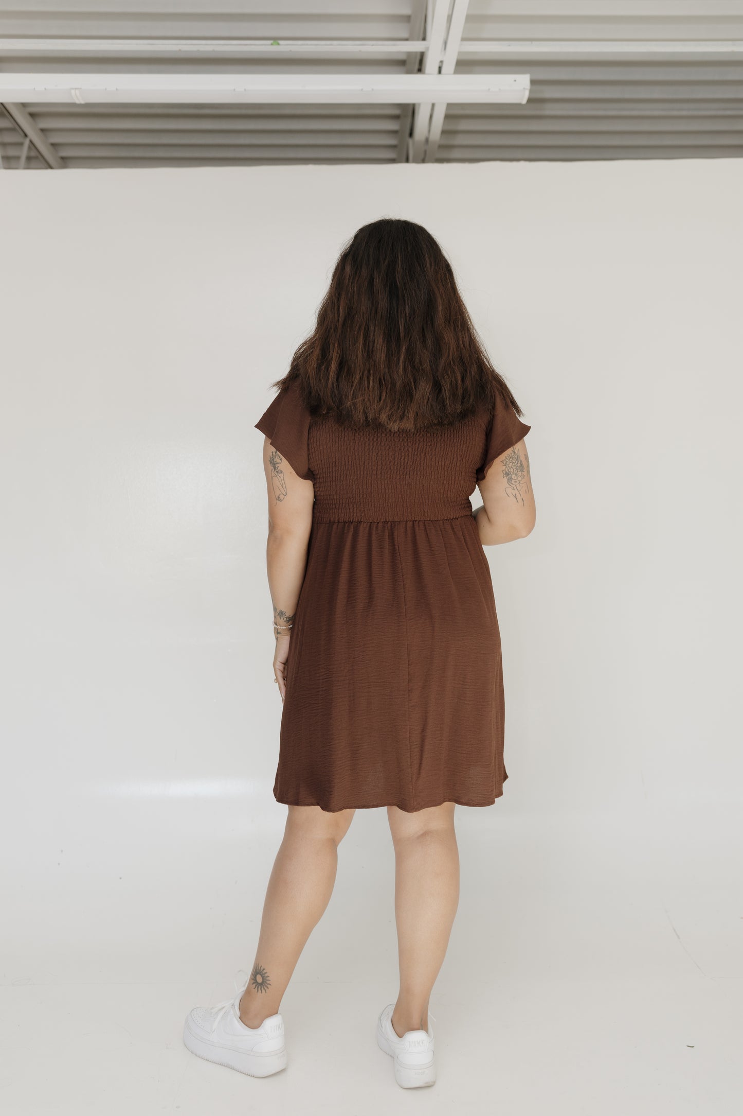 Person wearing a brown dress standing against a white wall