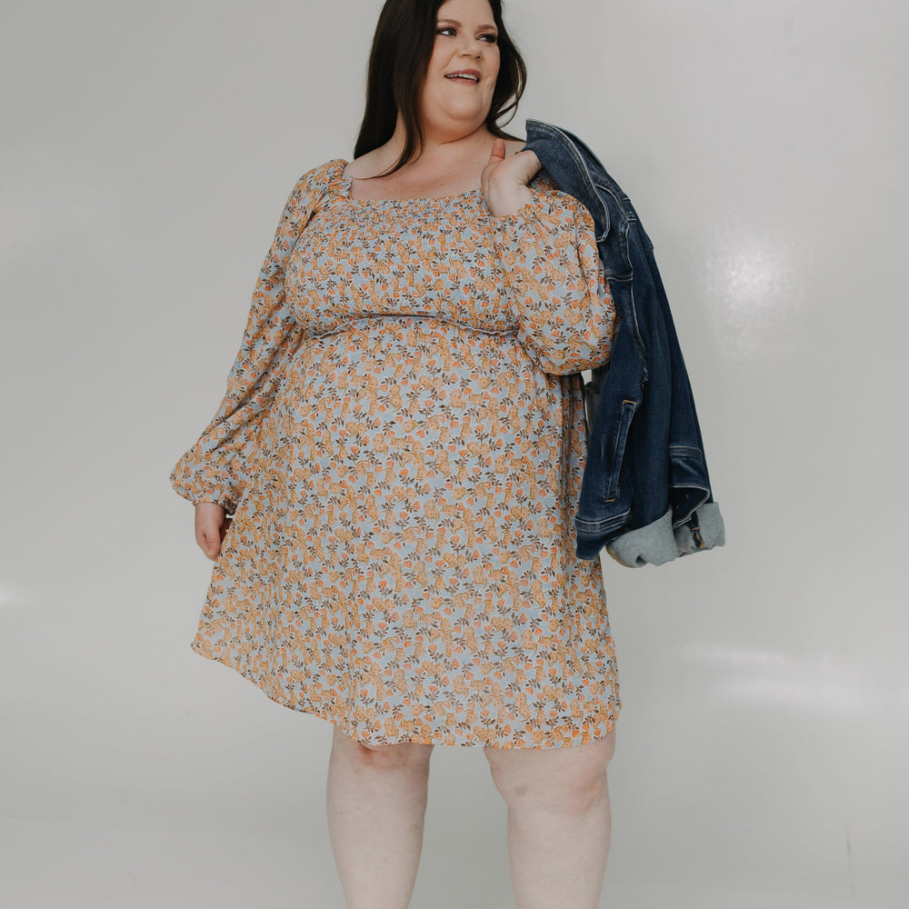 Woman wearing a floral dress with a denim jacket over her shoulder on a white background