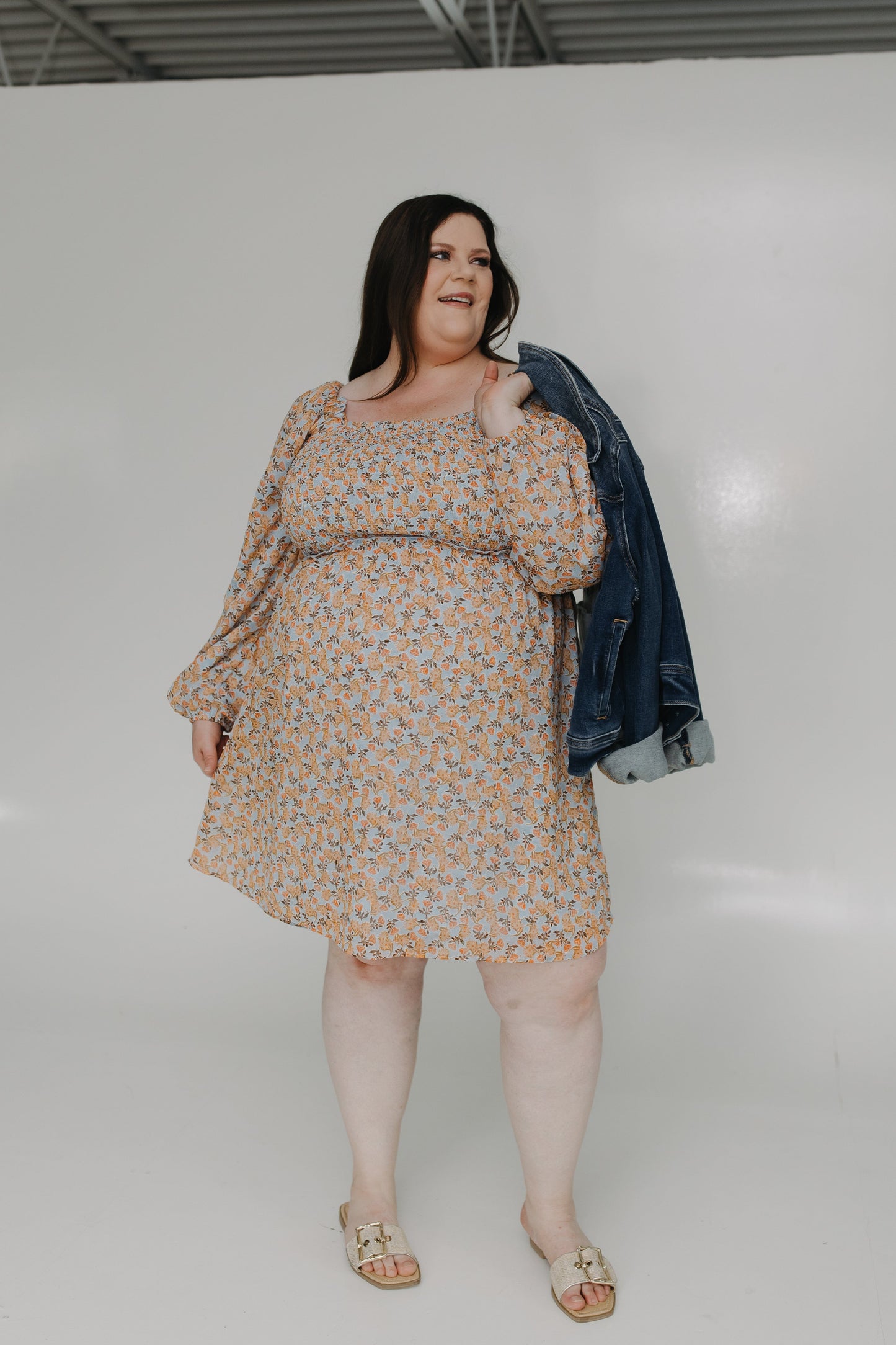 Woman wearing a floral dress with a denim jacket over her shoulder on a white background
