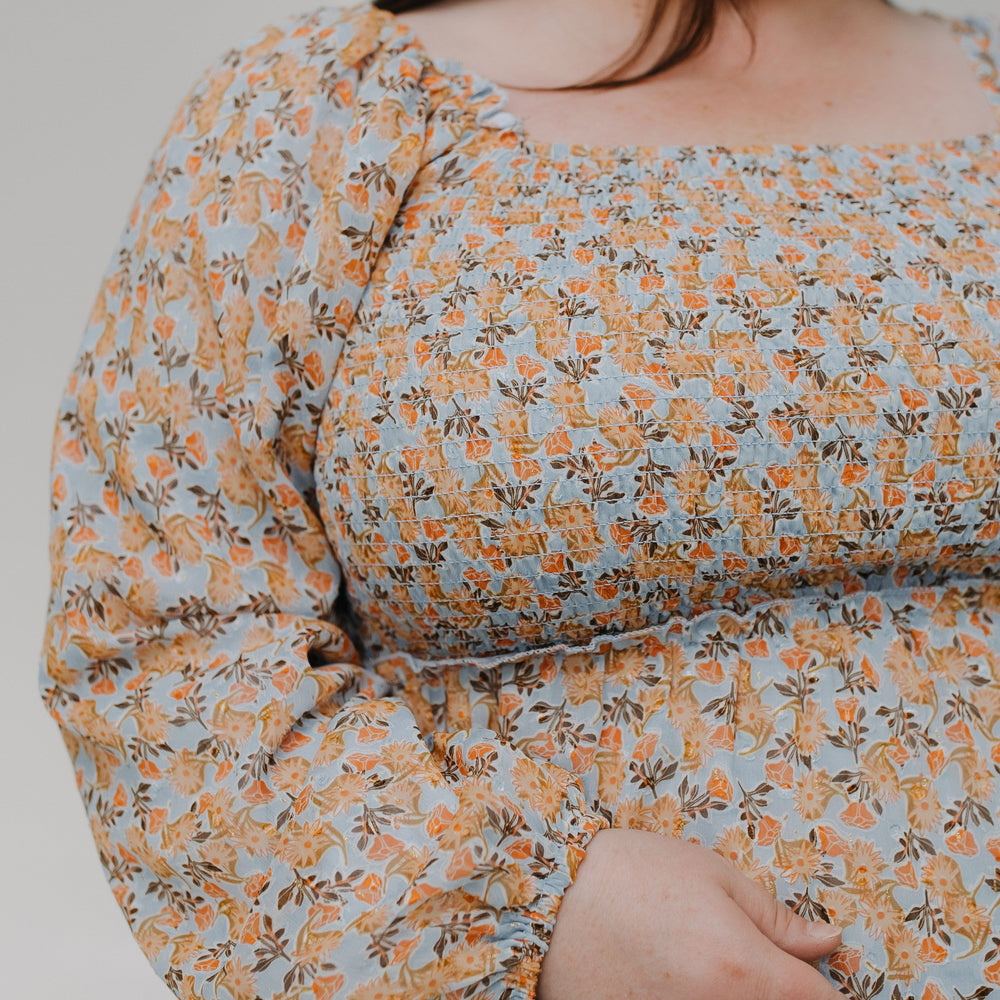 Person wearing a floral dress with long sleeves on a plain background