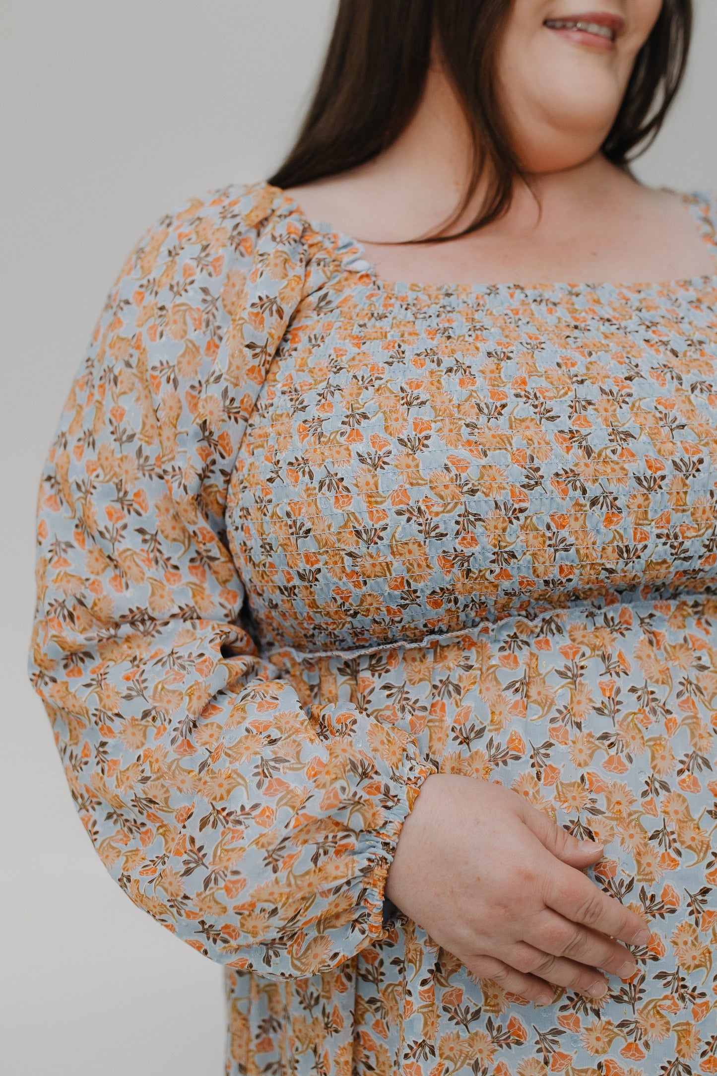 Person wearing a floral dress with long sleeves on a plain background