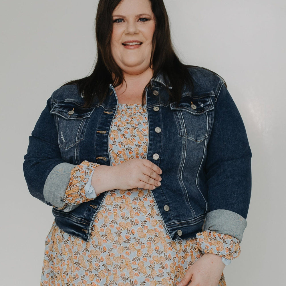 Woman wearing a floral dress with a denim jacket on a white background
