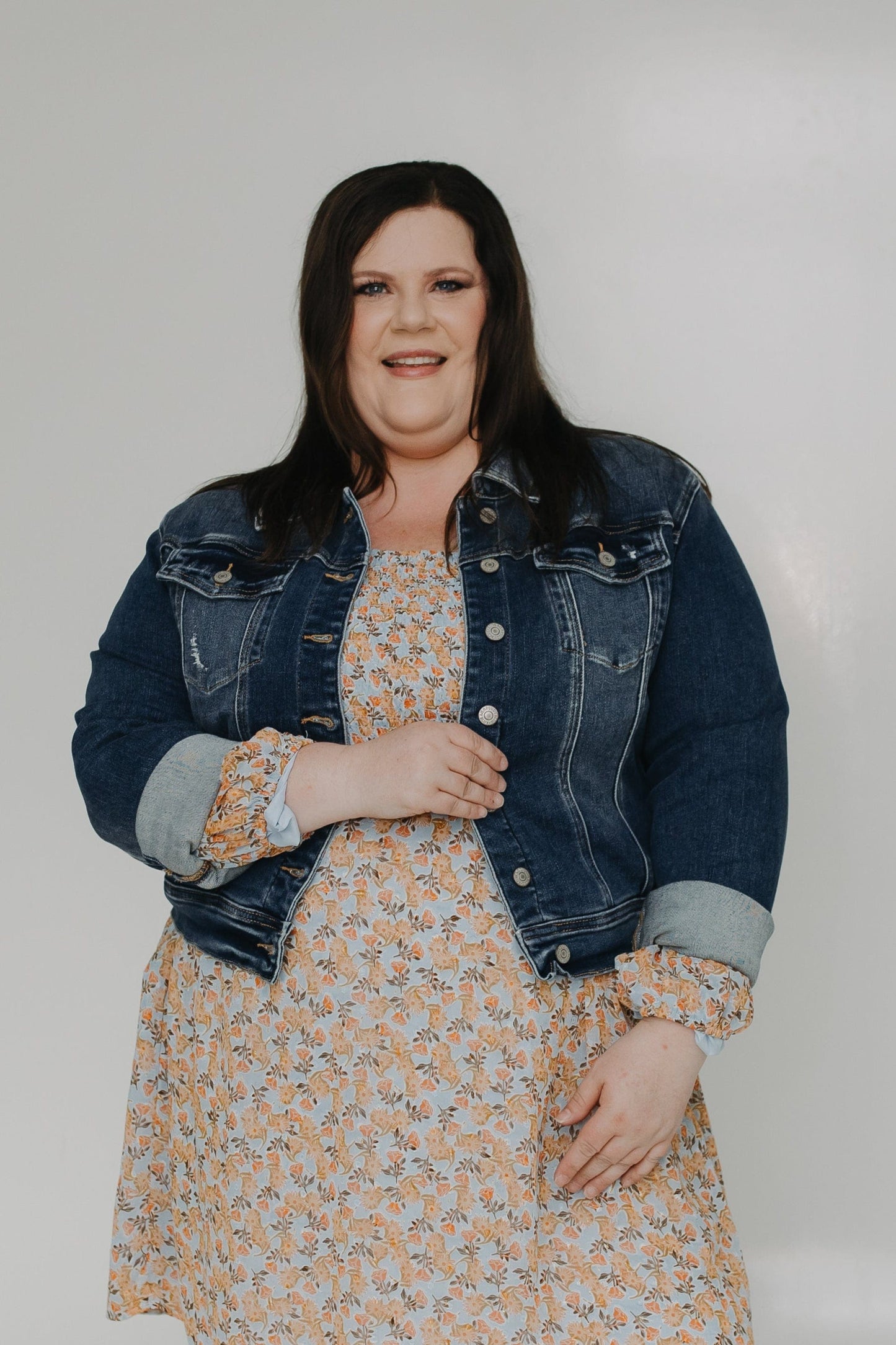 Woman wearing a floral dress with a denim jacket on a white background