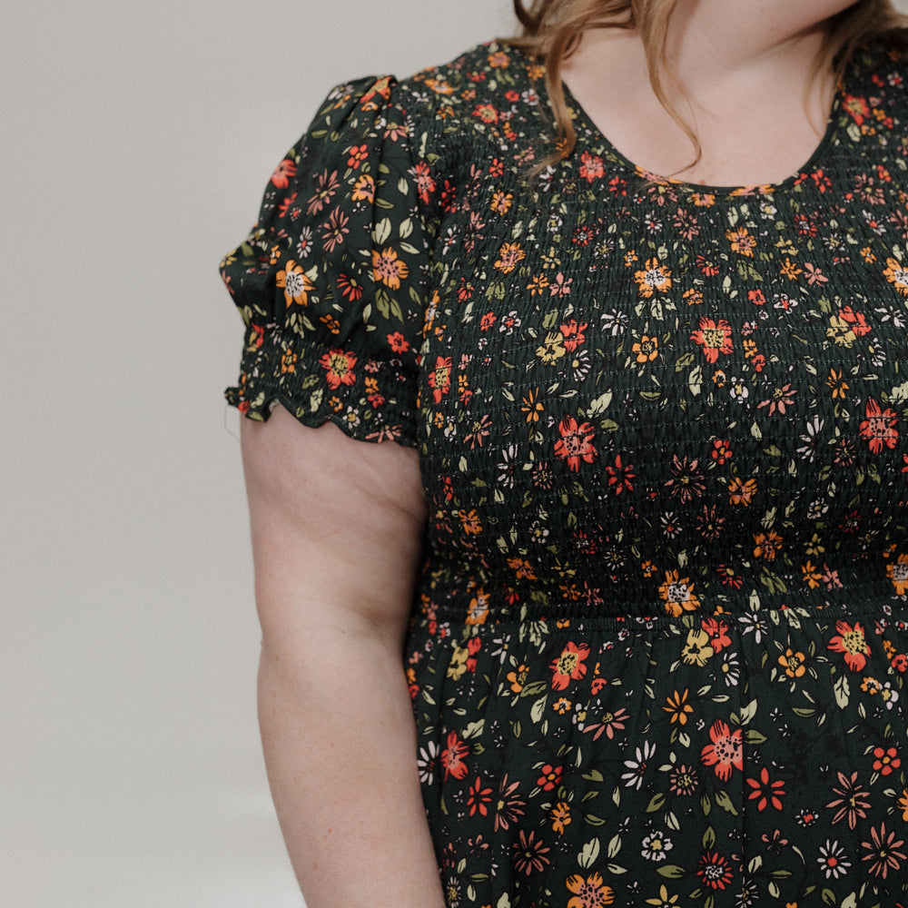 Woman wearing a black floral dress against a plain background