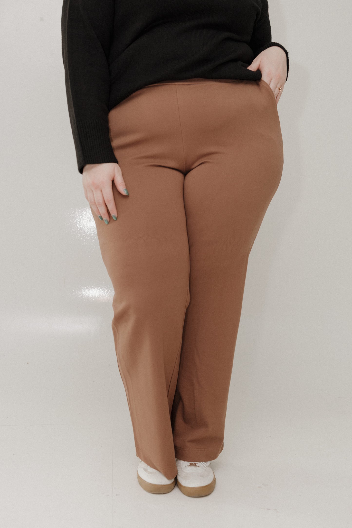 Person wearing brown pants and a black top on a white background