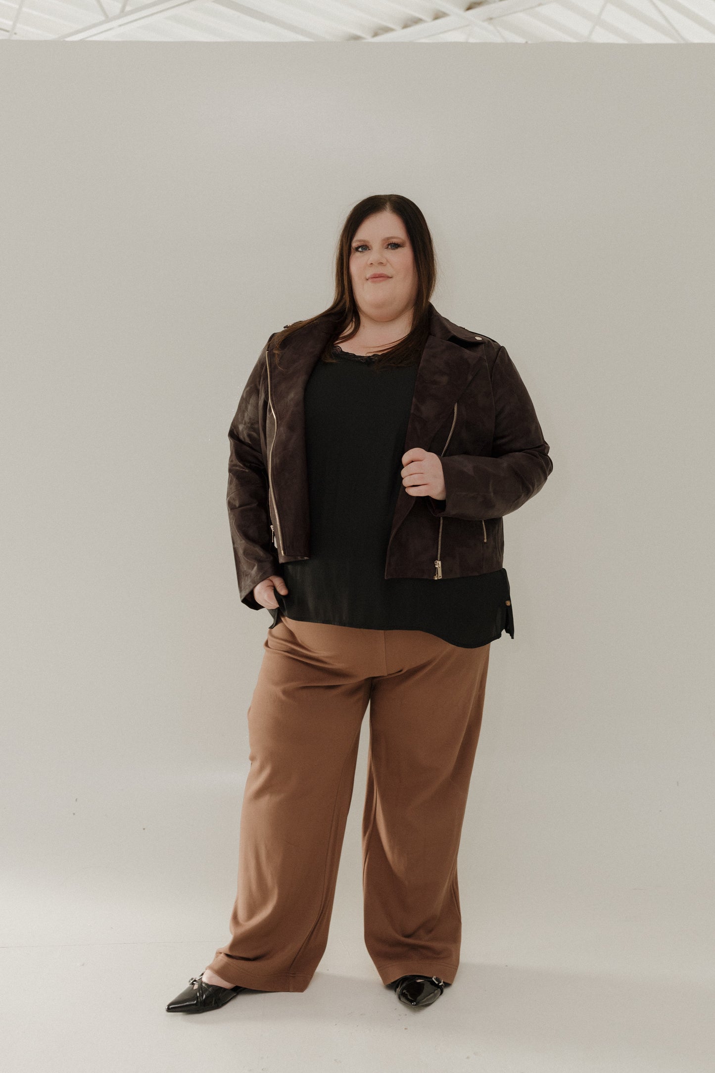 Person wearing a brown jacket and tan pants against a white background