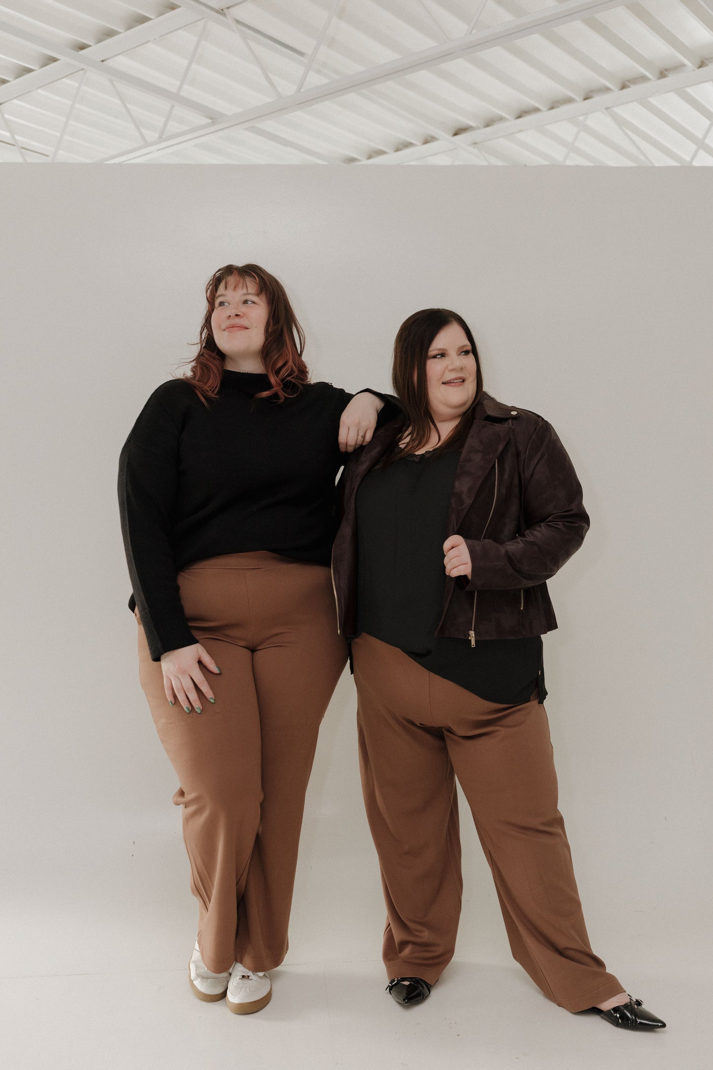 Two women standing side by side against a white wall.