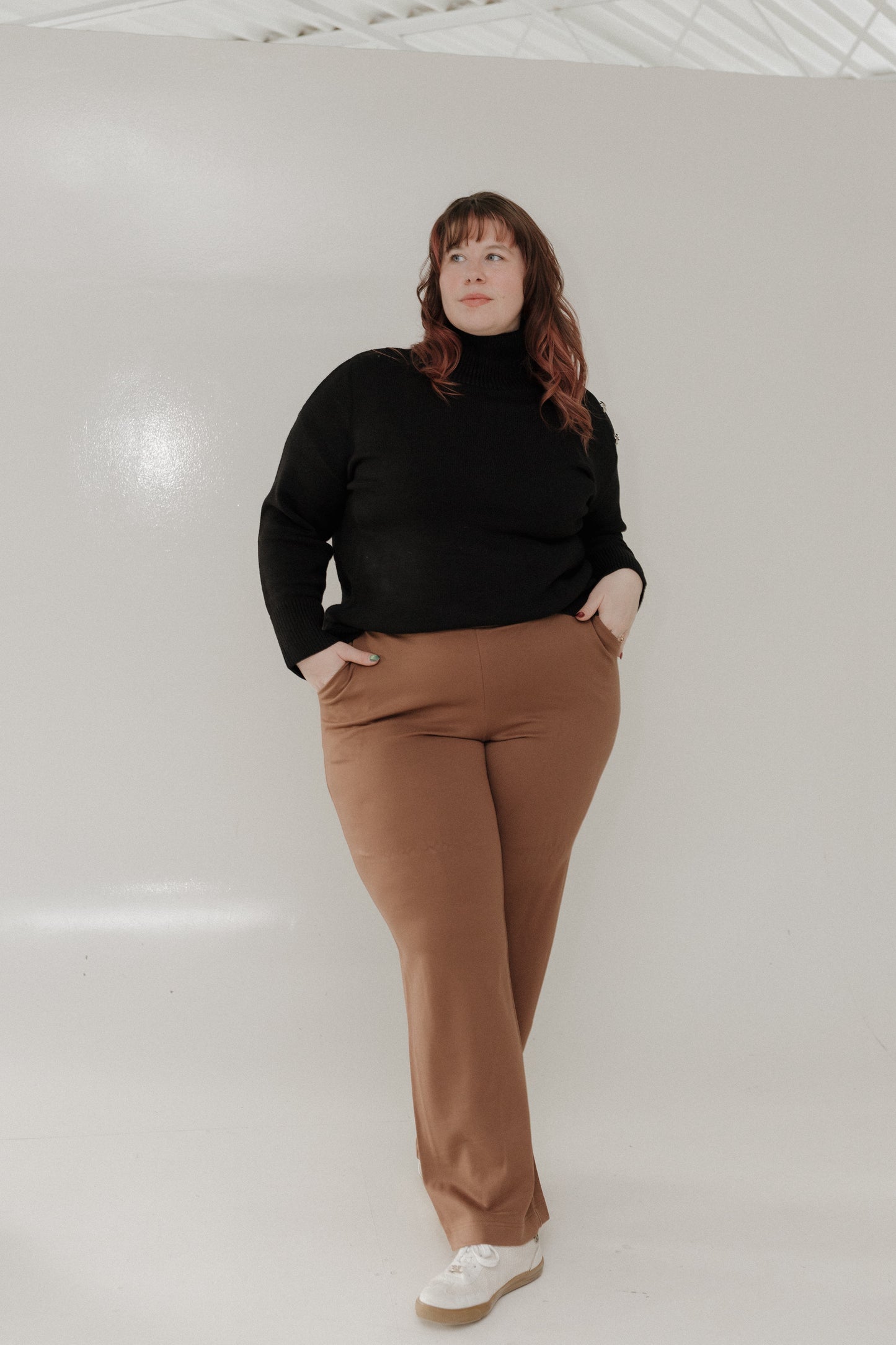 Person wearing a black turtleneck and brown pants on a white background