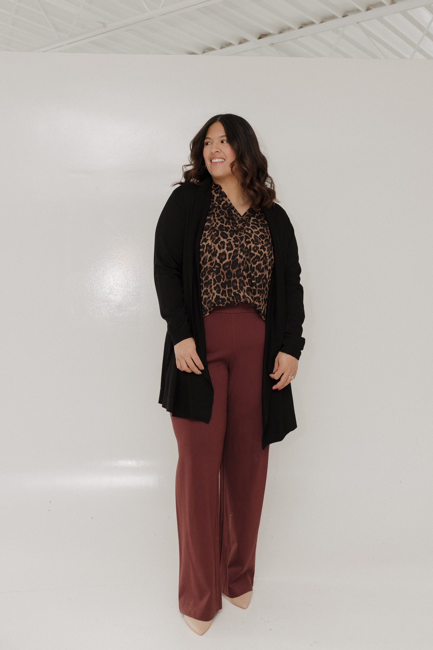 Woman wearing a black cardigan, leopard print top, and maroon pants against a white background