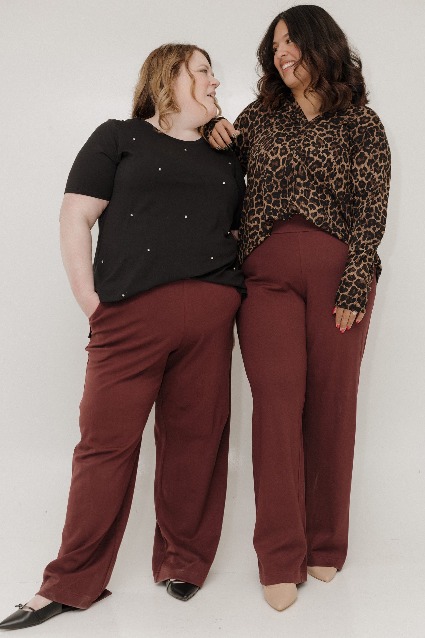Two women wearing matching outfits with black tops and maroon pants against a white background