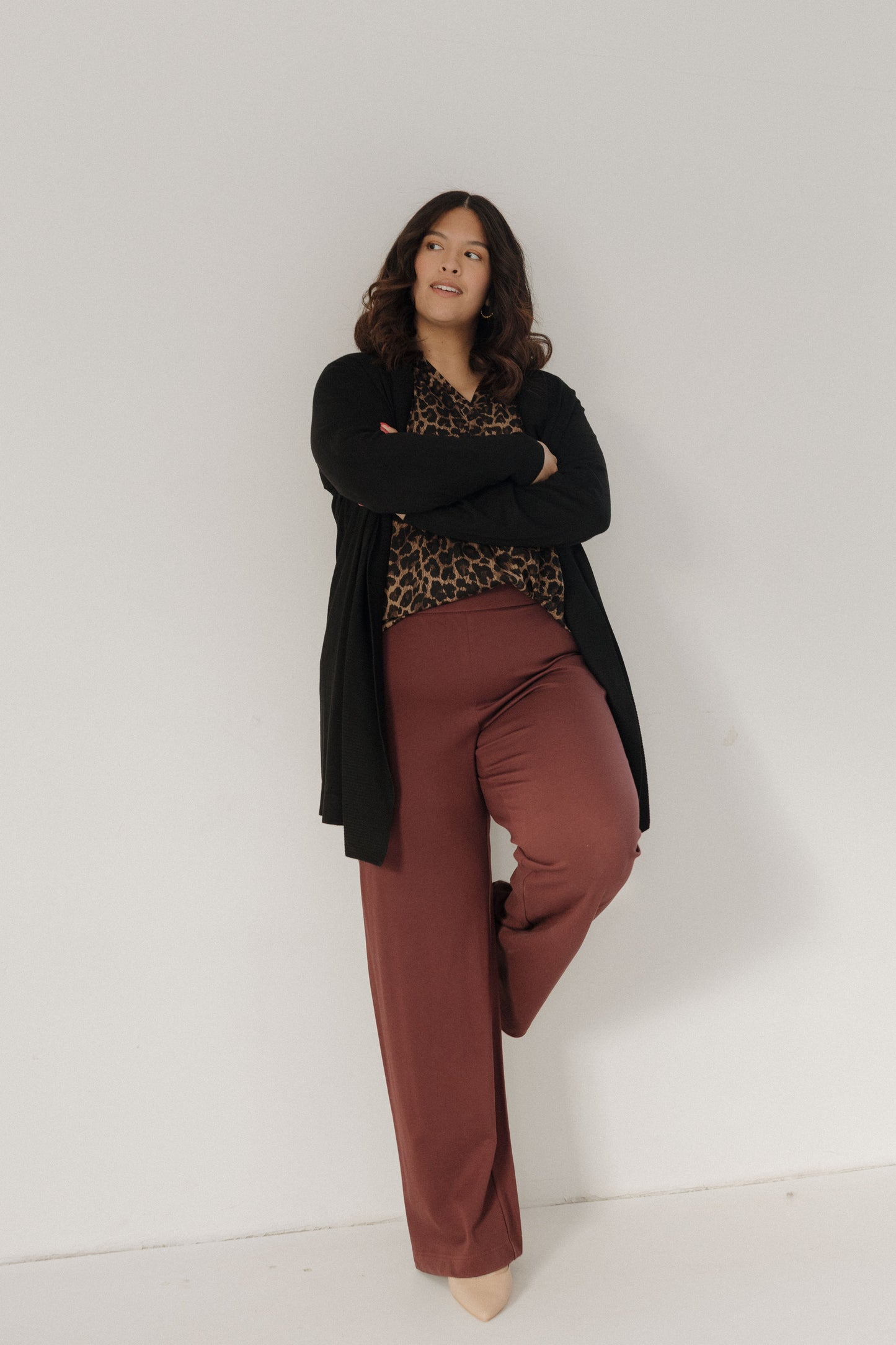 Woman wearing a black cardigan, leopard print top, and brown pants against a white background
