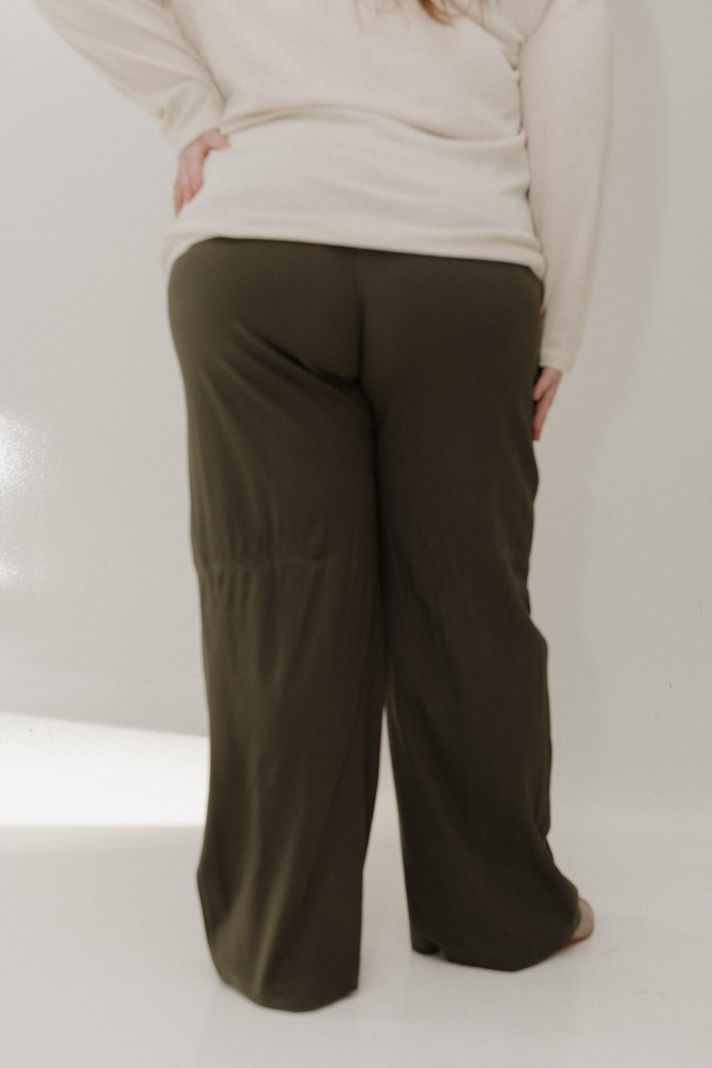 Person wearing olive green pants and a beige sweater on a white background