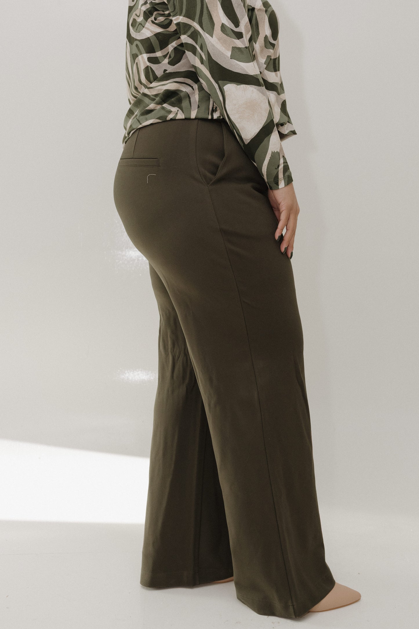 Person wearing olive green wide-leg pants and a patterned top on a white background
