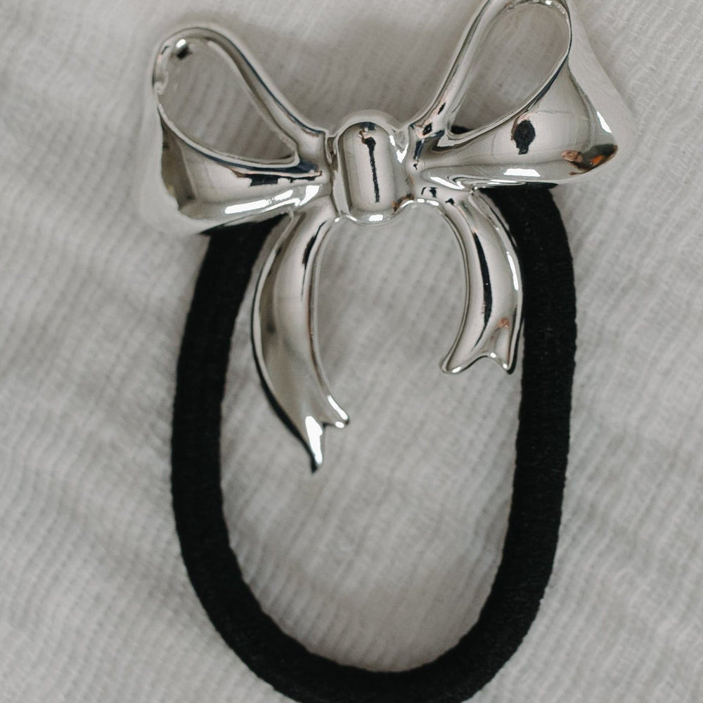 Silver bow-shaped hair tie on a gray background