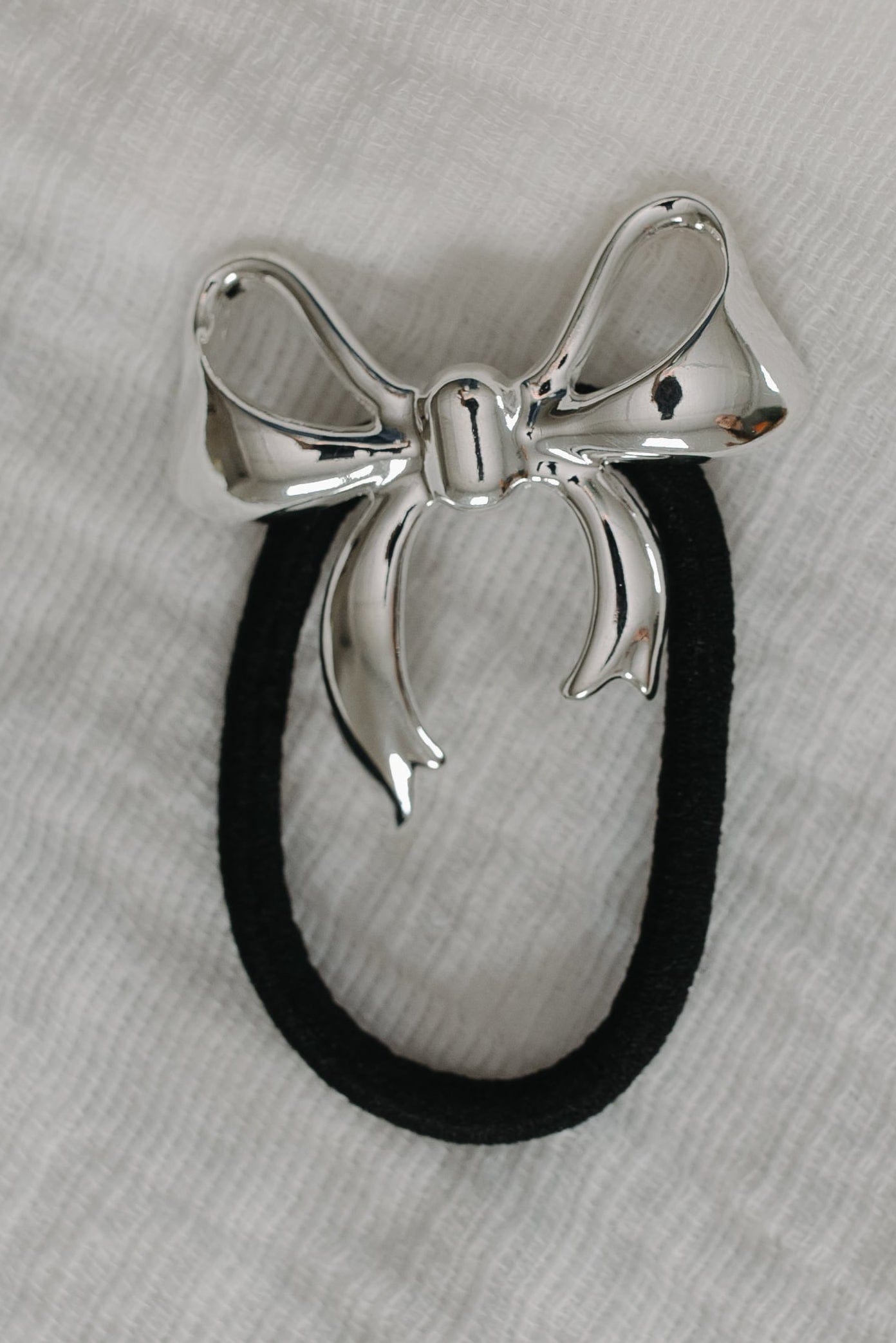 Silver bow-shaped hair tie on a gray background
