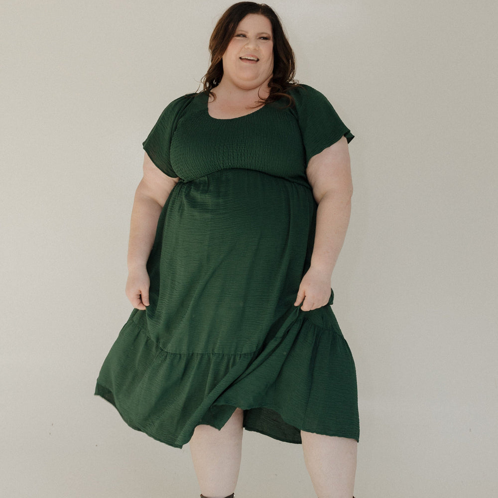 Woman wearing a green dress and brown boots against a plain background