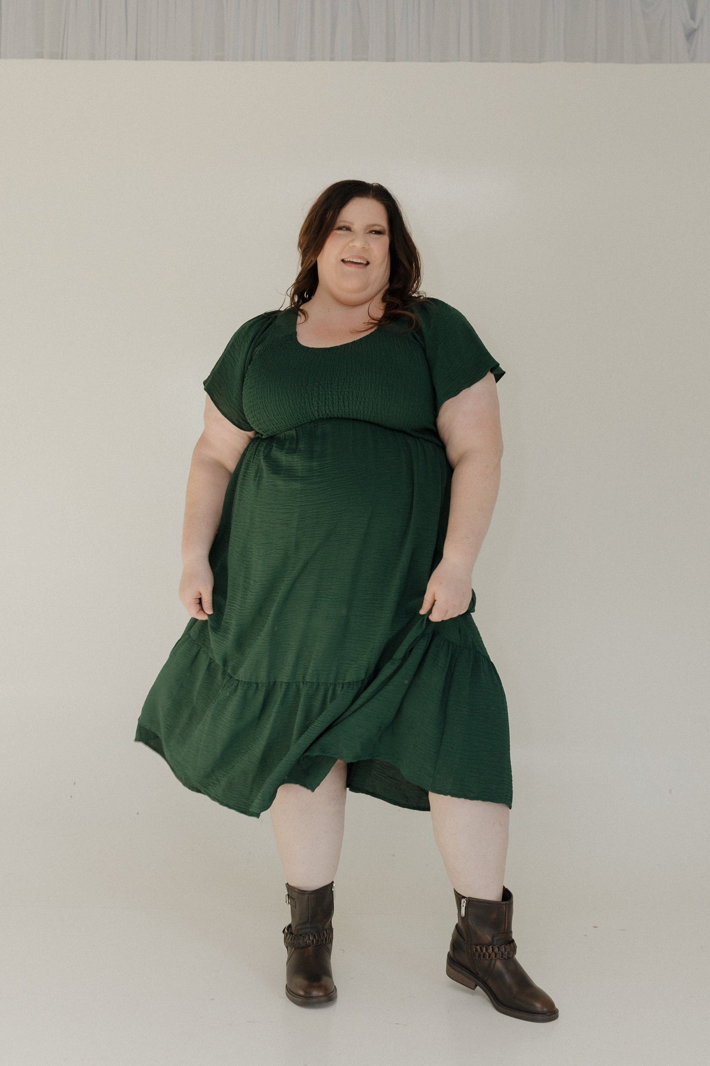 Woman wearing a green dress and brown boots against a plain background