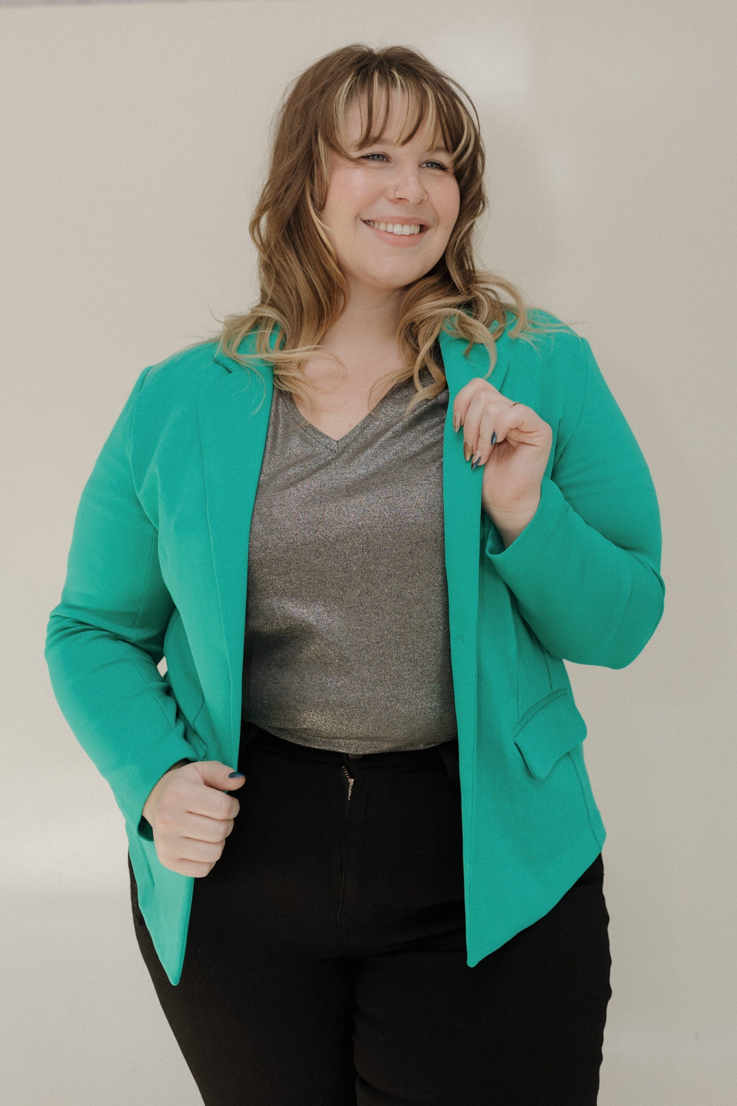 Woman wearing a teal blazer over a gray top and black pants on a plain background