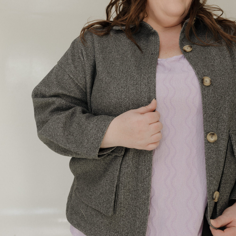 Woman wearing a gray jacket over a light purple top against a plain background