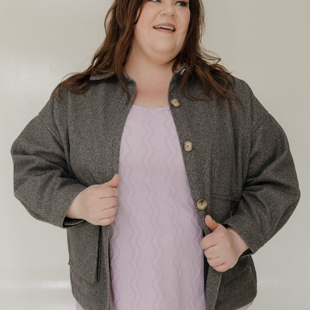 Woman wearing a gray jacket over a light purple top against a plain background