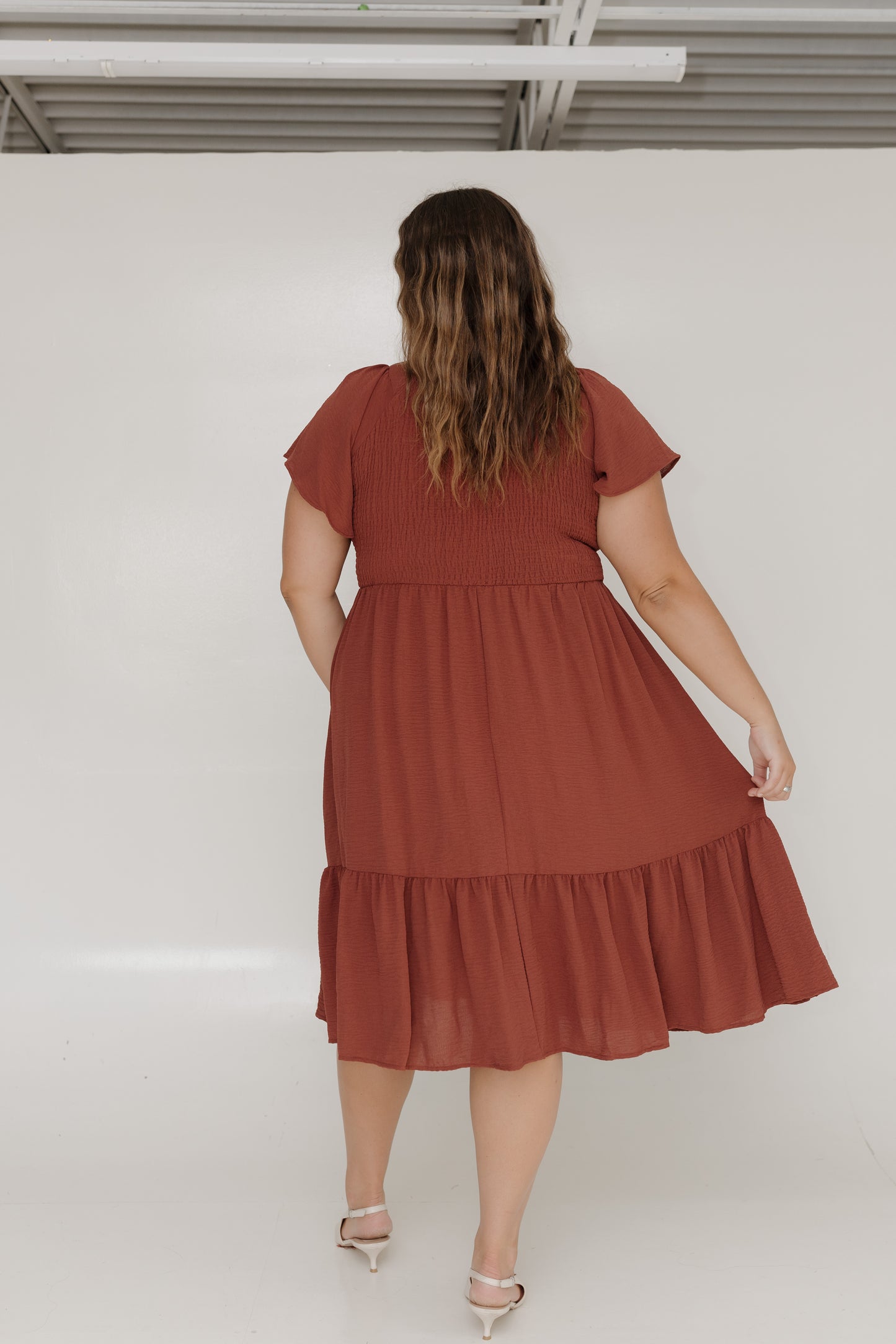 Woman wearing a rust-colored dress against a white wall