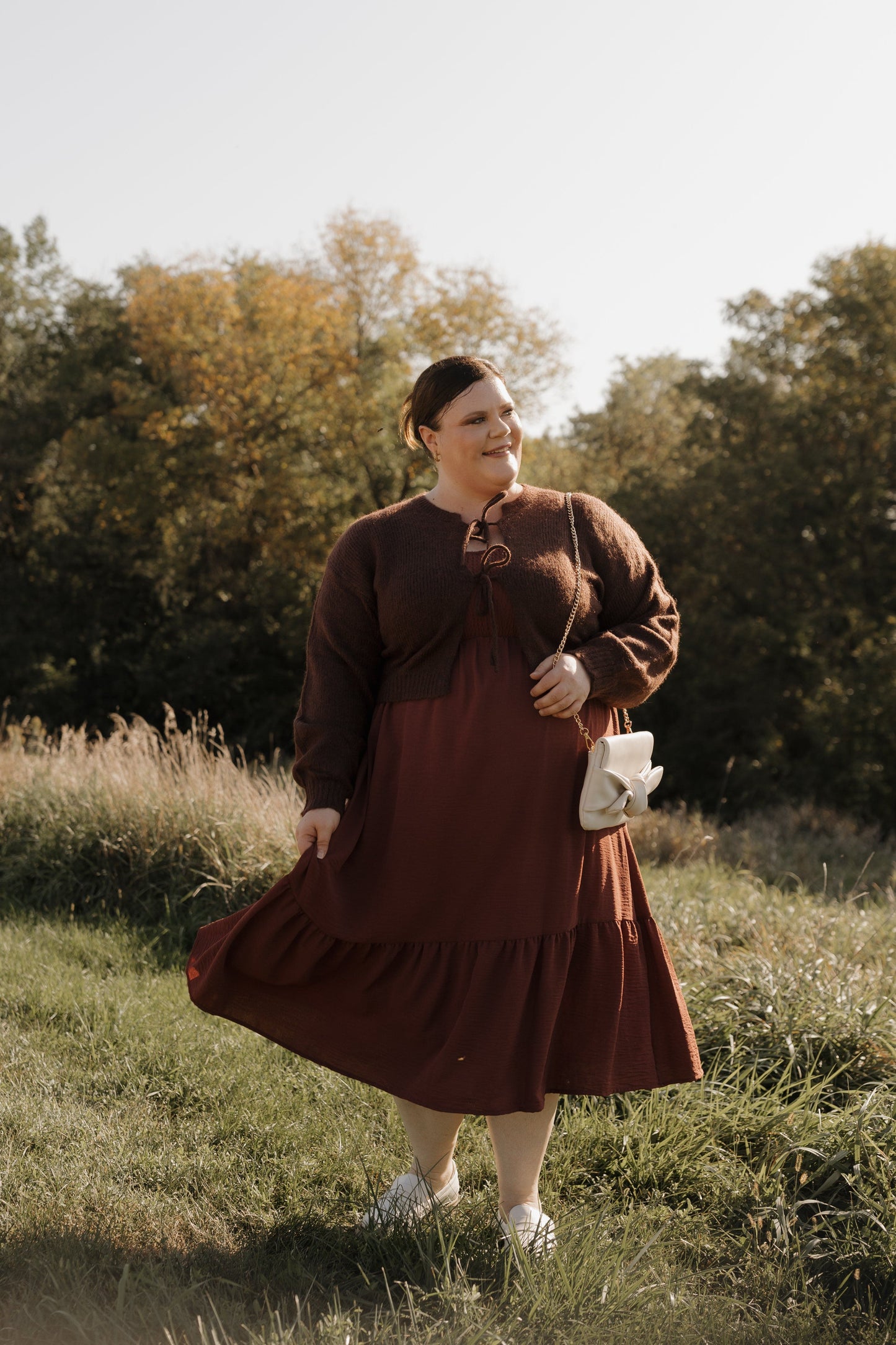 Woman in a brown dress standing in a field with trees in the background