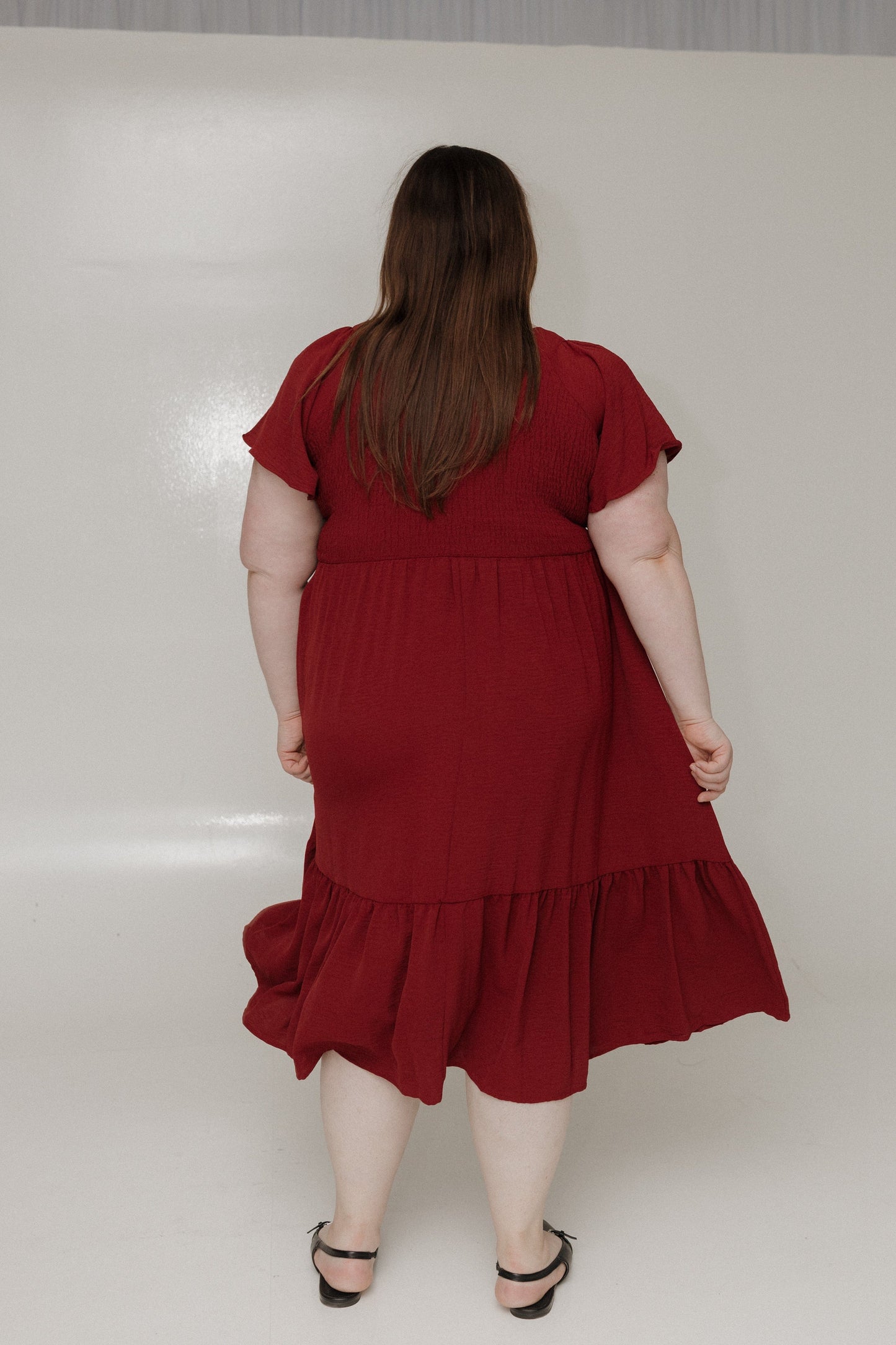 Person wearing a red dress with ruffled layers on a white background