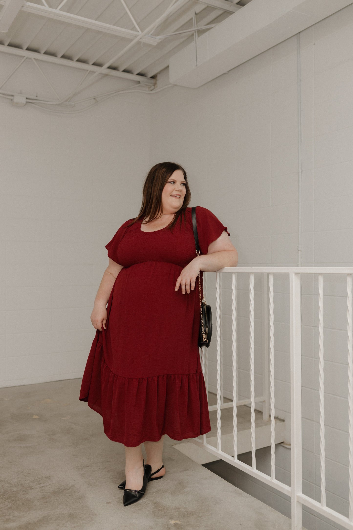 Woman in a red dress standing in an indoor setting with white walls and a metal railing.