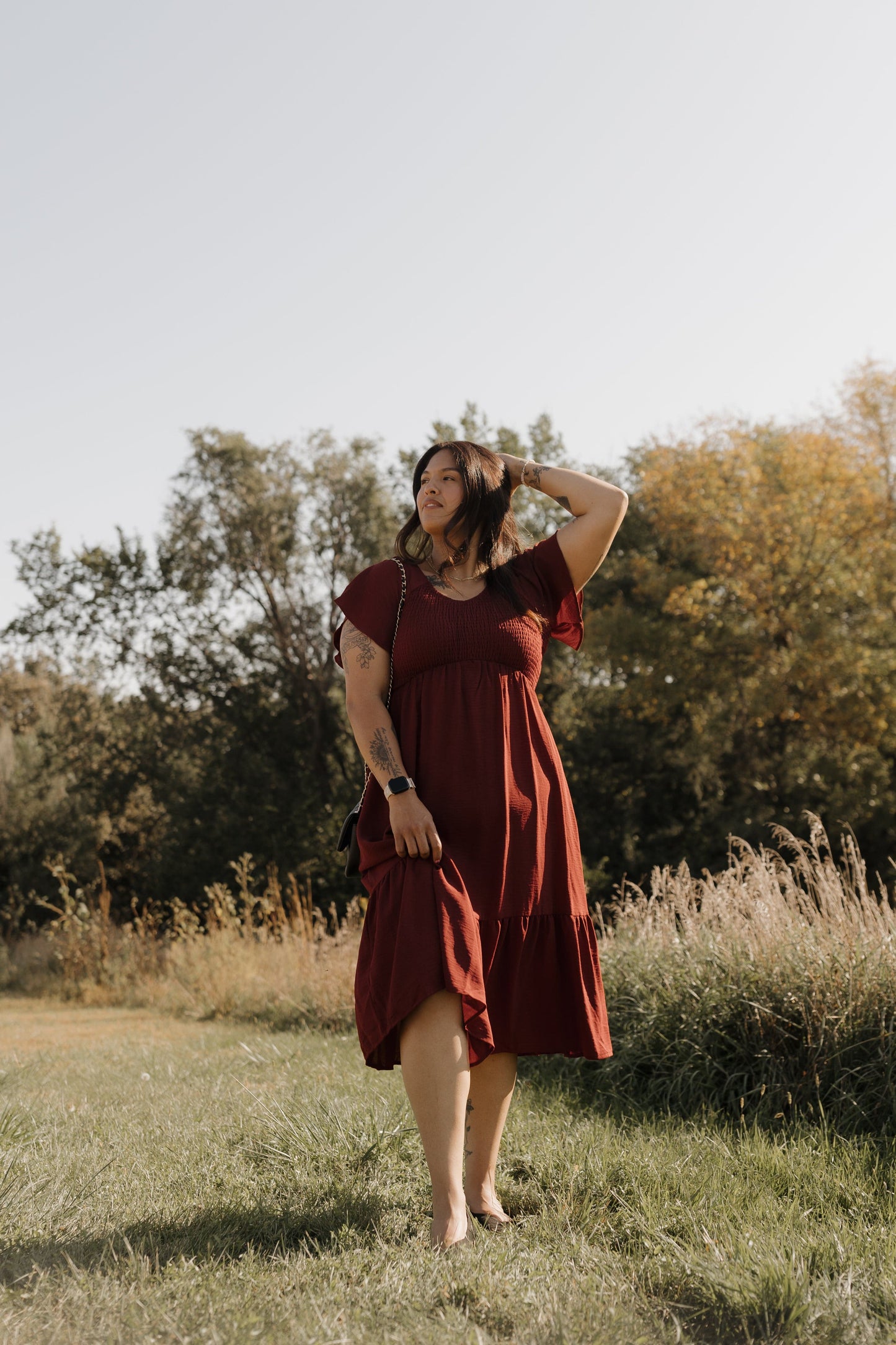Woman in a red dress standing in a field with trees in the background