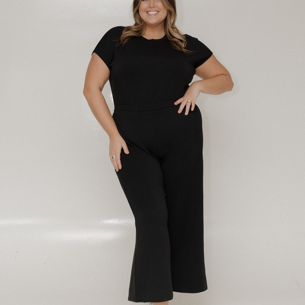 Woman wearing a black outfit with white sneakers on a plain background