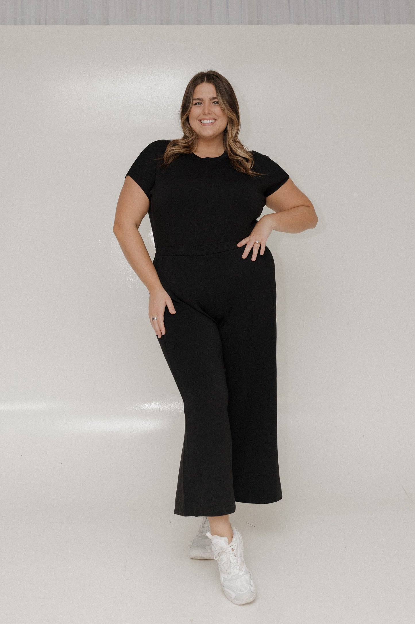 Woman wearing a black outfit with white sneakers on a plain background