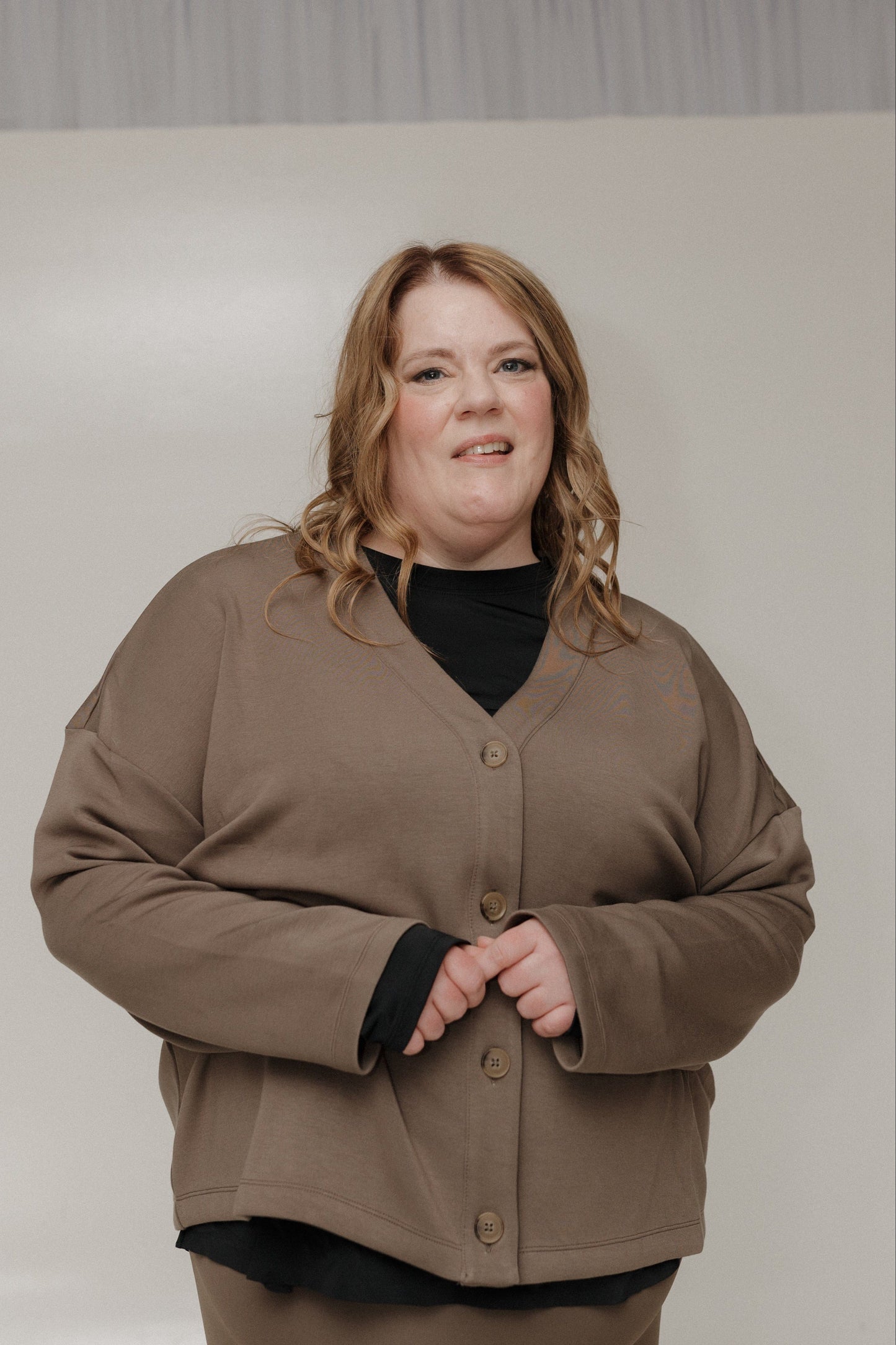 Person wearing a brown jacket and black shirt against a plain background