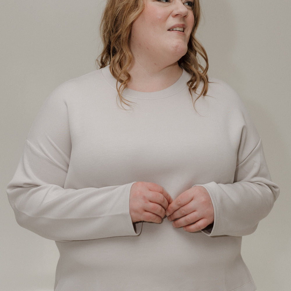 Person wearing a light gray sweatshirt and pink pants against a plain background
