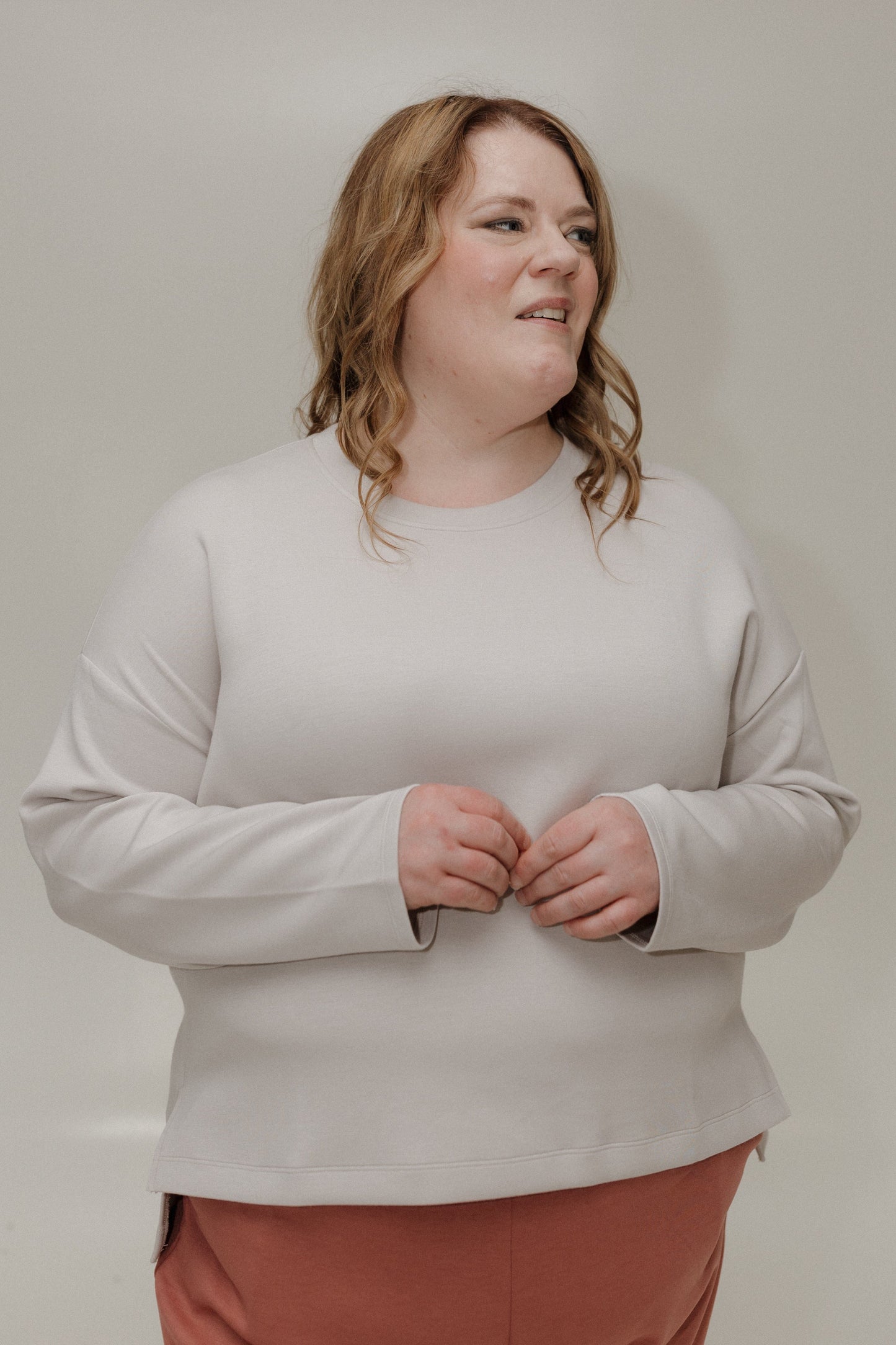 Person wearing a light gray sweatshirt and pink pants against a plain background