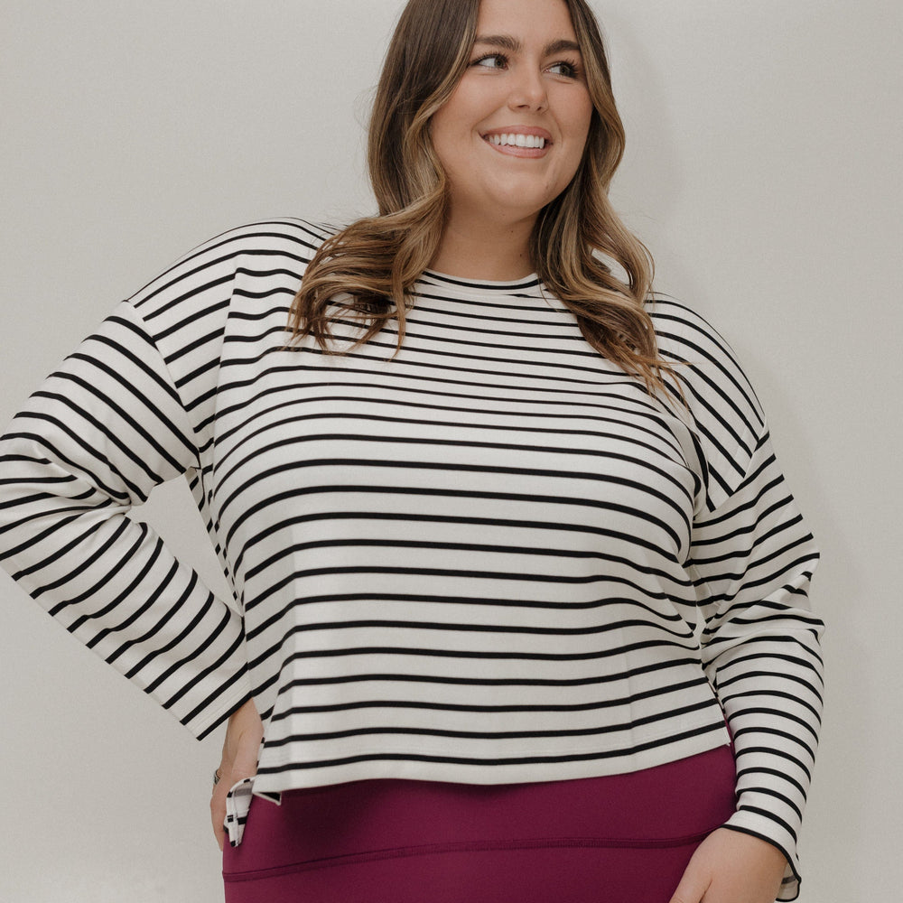 Woman wearing a black and white striped sweater and pink pants against a plain background