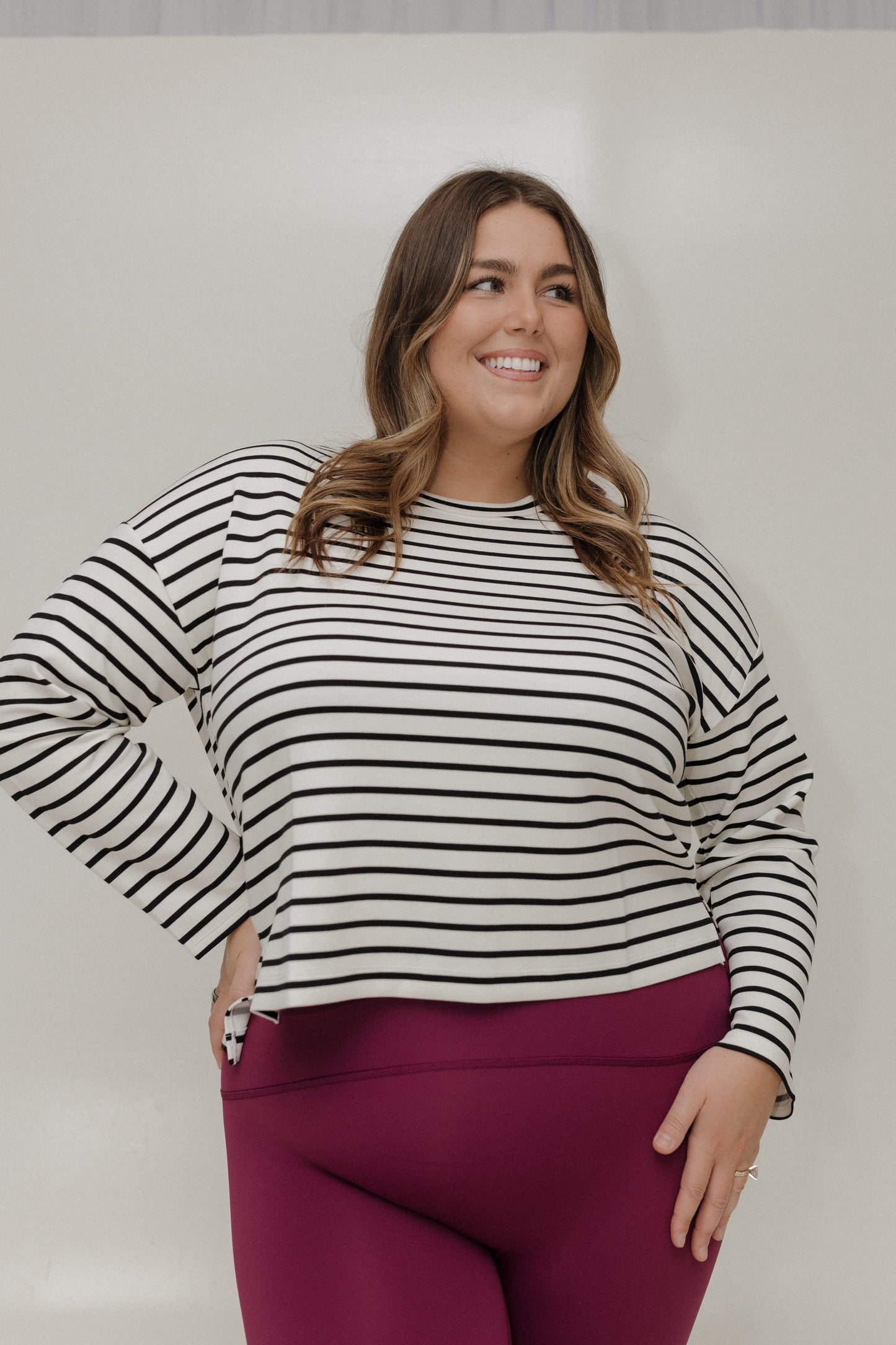Woman wearing a black and white striped sweater and pink pants against a plain background