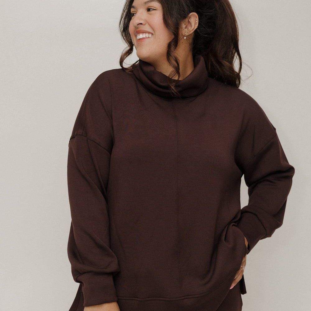 Woman wearing a brown sweatshirt and pants against a plain background