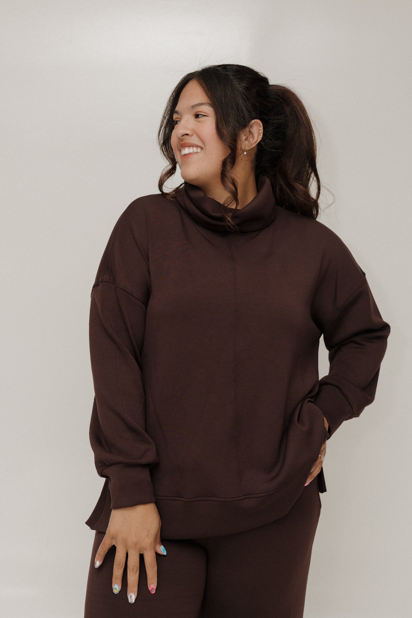 Woman wearing a brown sweatshirt and pants against a plain background