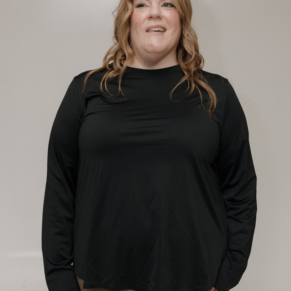 Woman wearing a black long-sleeve top and brown pants against a plain background