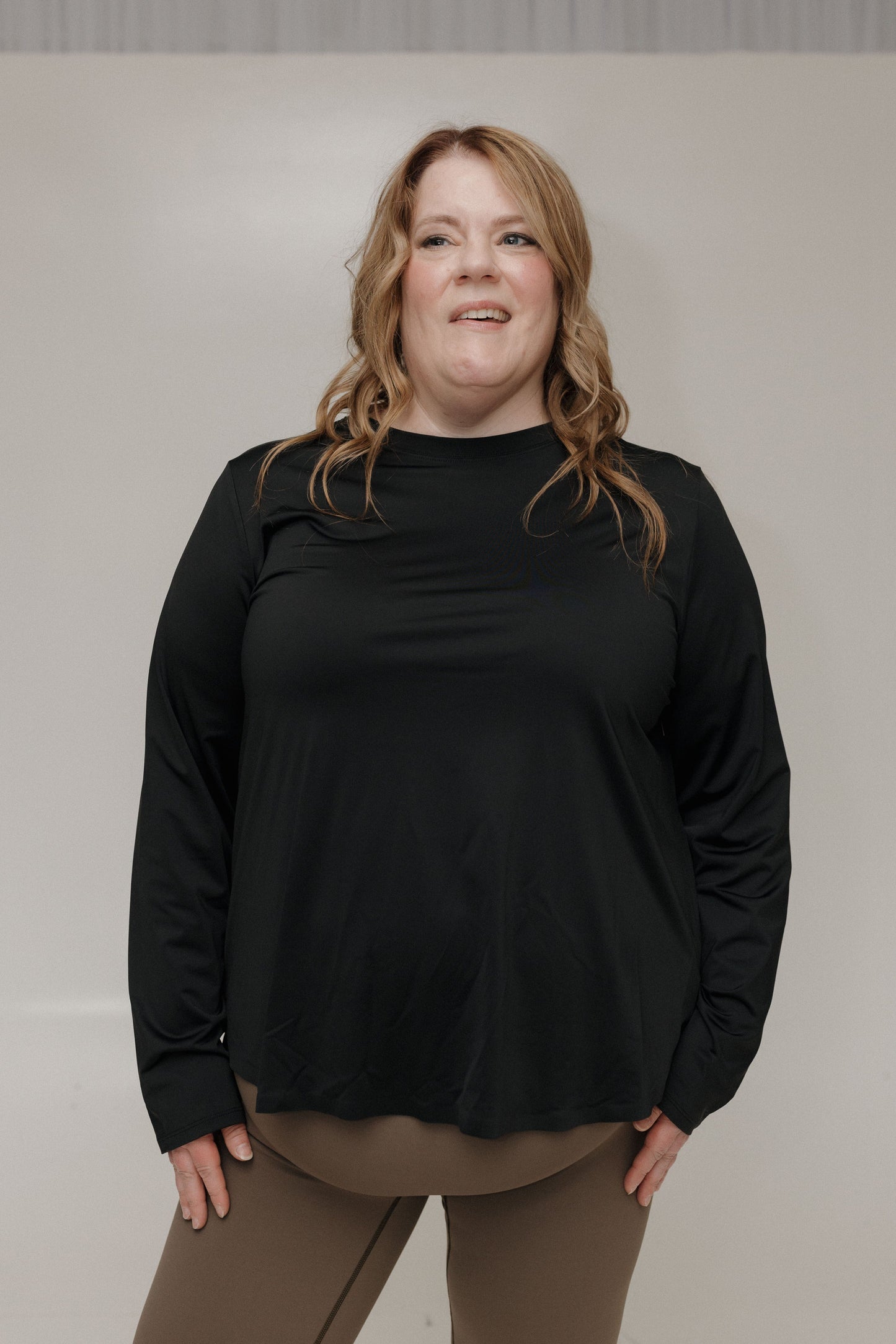 Woman wearing a black long-sleeve top and brown pants against a plain background