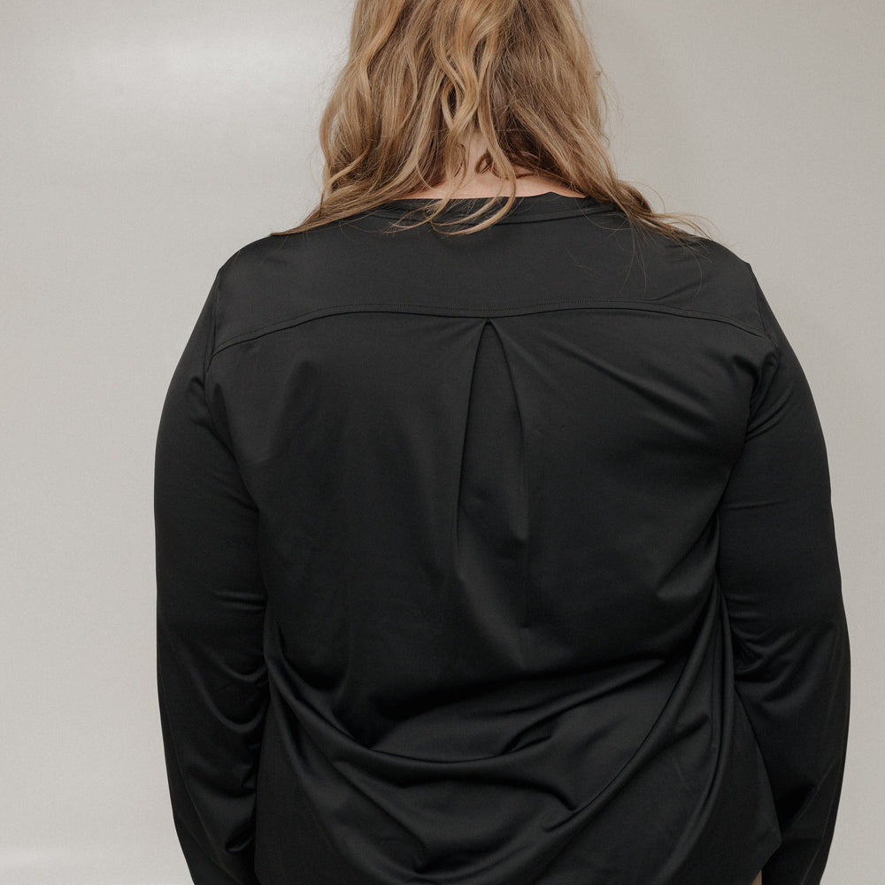 Person wearing a black long-sleeve top with a pleated design on a plain background