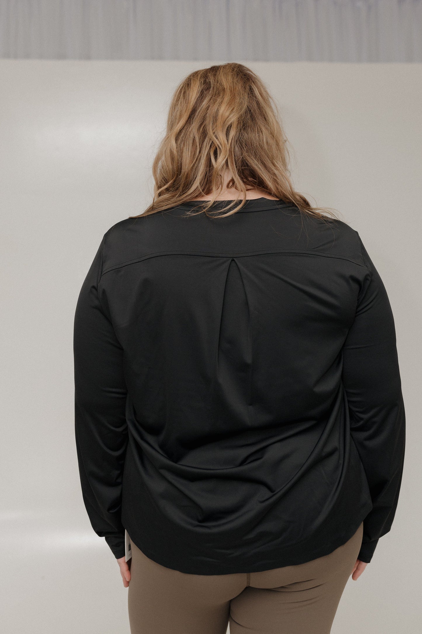 Person wearing a black long-sleeve top with a pleated design on a plain background