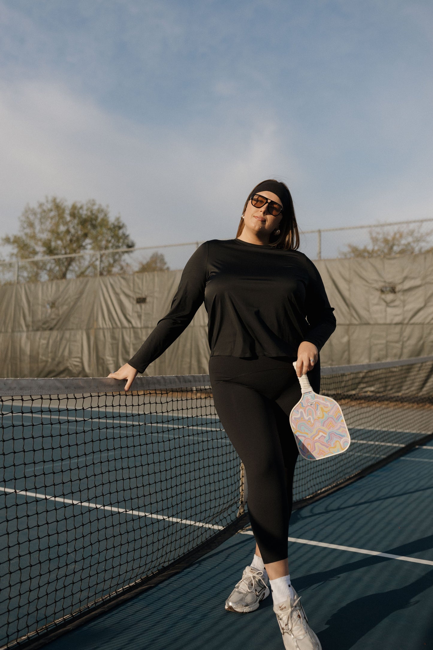 Person on a tennis court holding a paddle, wearing black athletic wear.