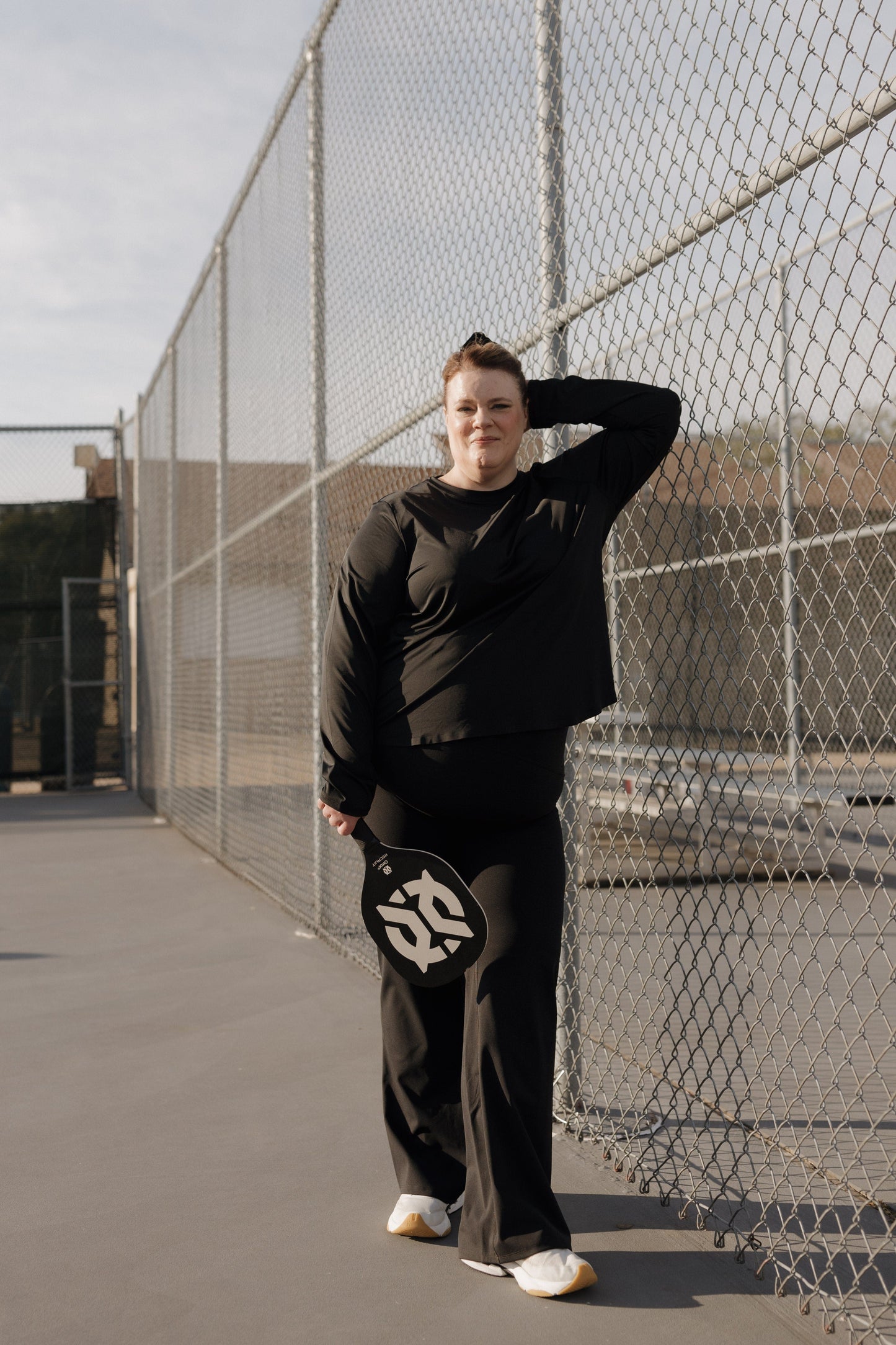 Person in black outfit holding a paddle against a chain-link fence.